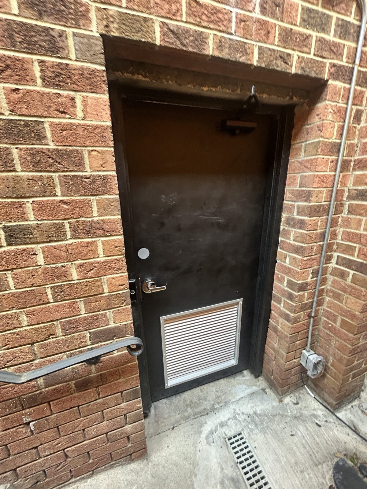 Plain black unmarked door at the bottom of the stairs, with a ventilation grille near the bottom.